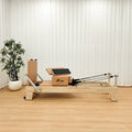 Oak-look natural wood Pilates reformer with tan cushions, shown in a studio