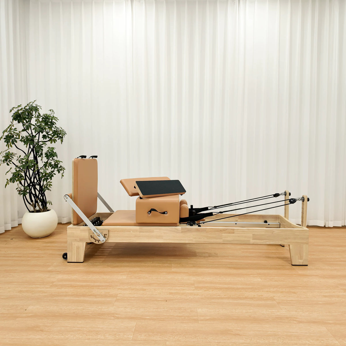 Oak-look natural wood Pilates reformer with tan cushions, shown in a studio